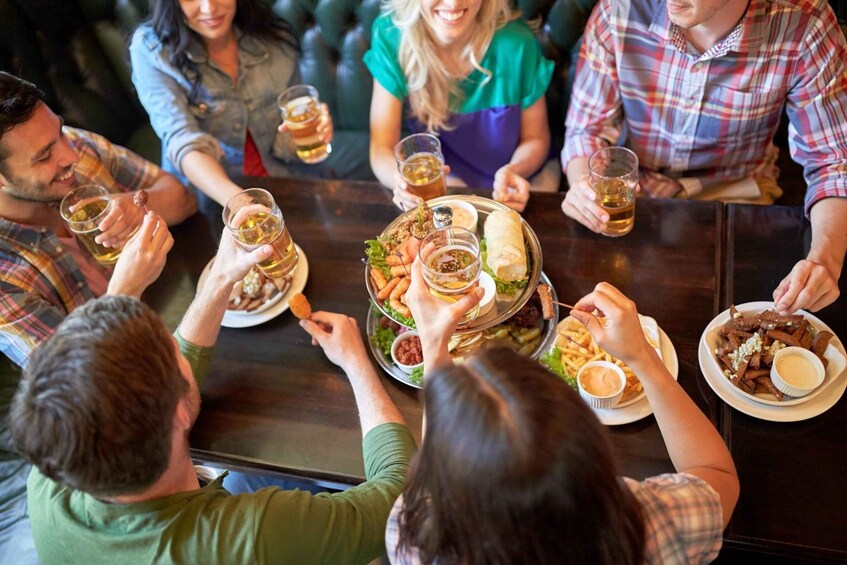 A group of people sitting around a table, holding drinks and eating various dishes. 5
