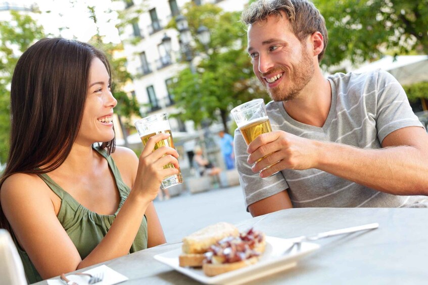 Two people toasting with beer glasses at an outdoor cafe. 1