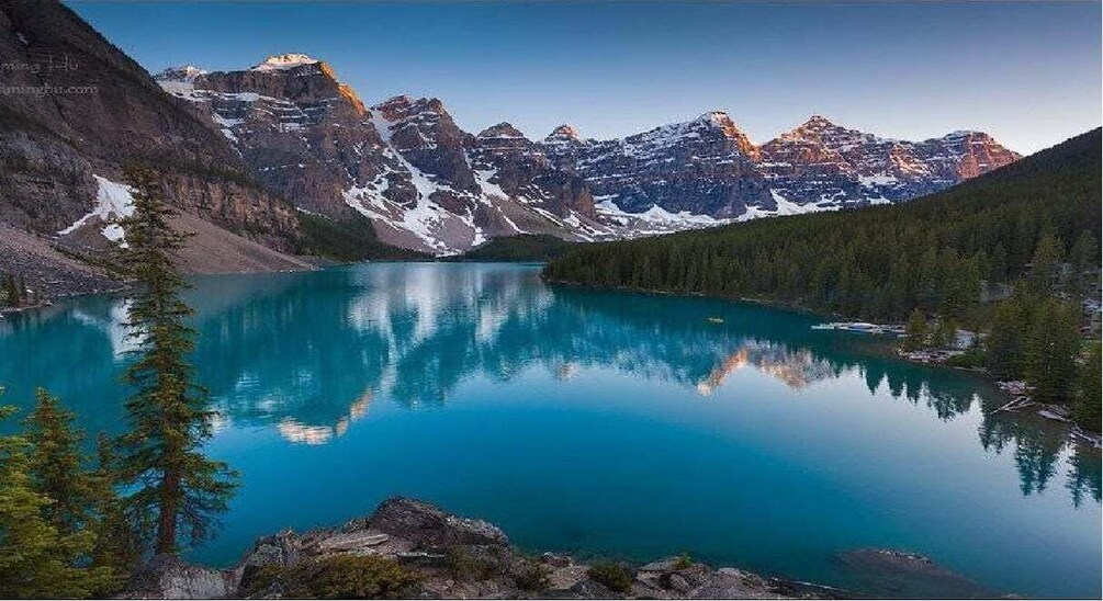 A mountain lake with clear reflections, surrounded by snow-capped peaks and dense forest. 2