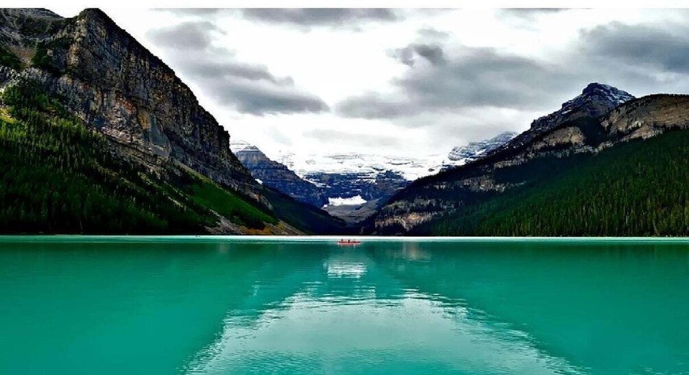 A turquoise lake surrounded by mountains with a boat in the center. 1