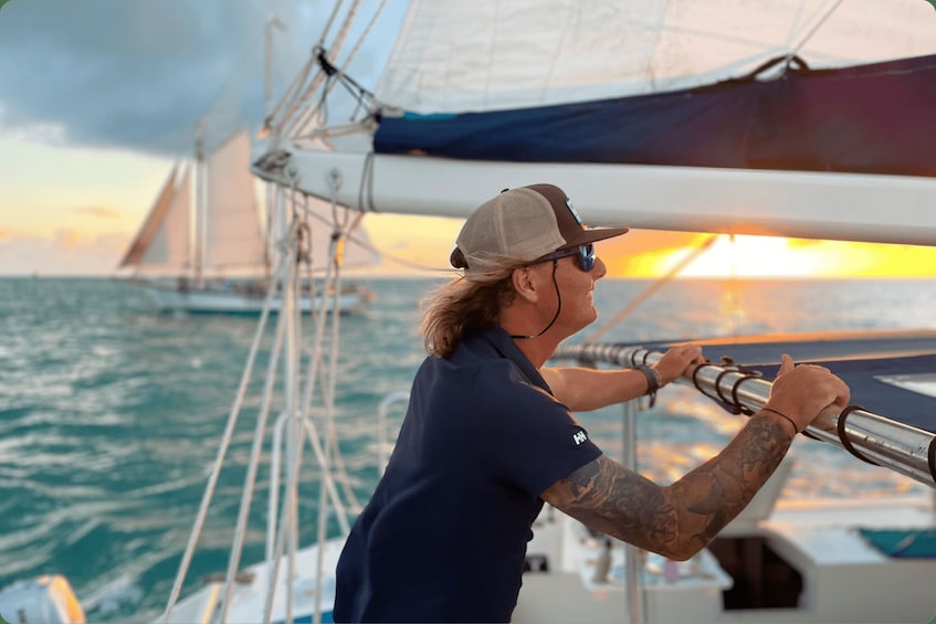 A person on a sailboat holding a rope, with a sunset in the background. 1