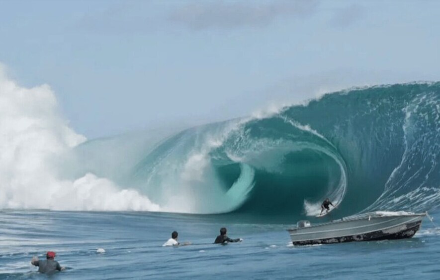 A large wave with a surfer riding it and a boat nearby. 1