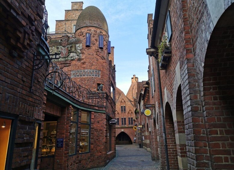 A narrow cobblestone street flanked by historic brick buildings with arched doorways and a distinctive tower with a dome. 4