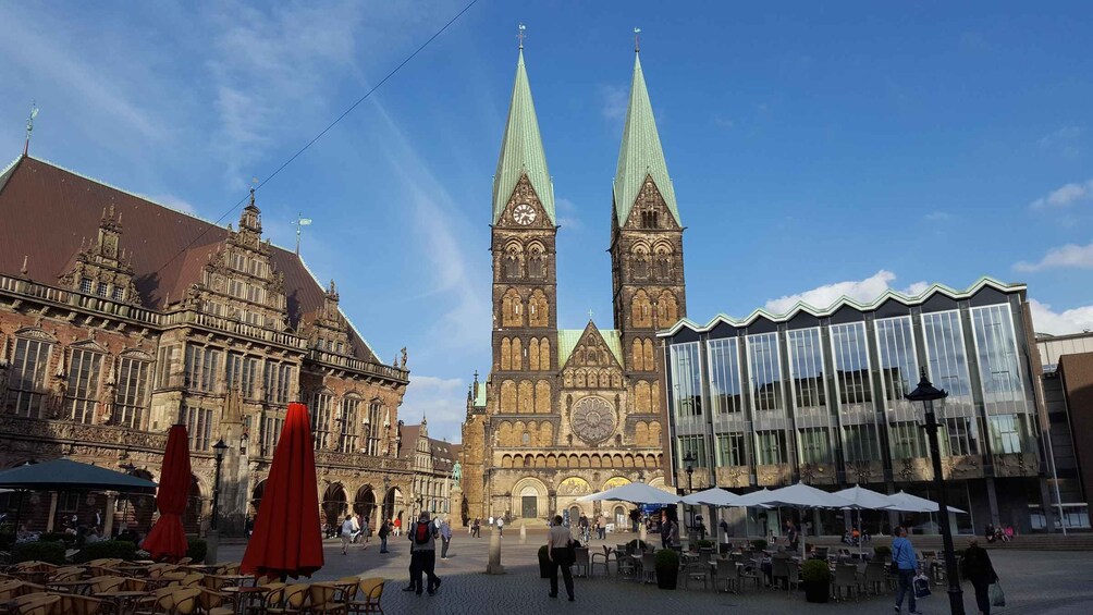 A historic building with two tall spires, a modern glass structure, and outdoor seating areas. 2
