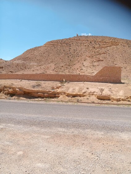 A desert landscape with a large, flat-topped hill and a paved road in the foreground. 2