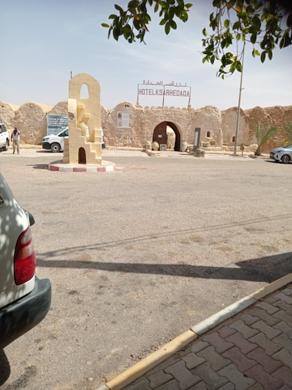 A desert landscape with a large archway and a sign for 'HOTELKSARHEEDA'. 4