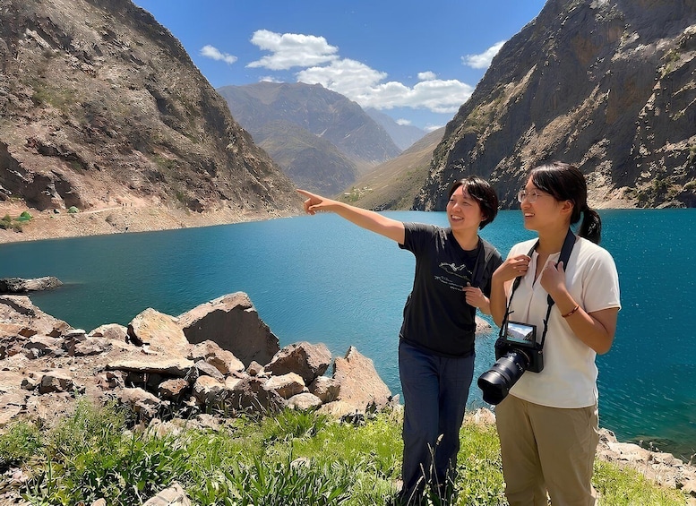 Two people standing by a lake with mountains in the background. 1