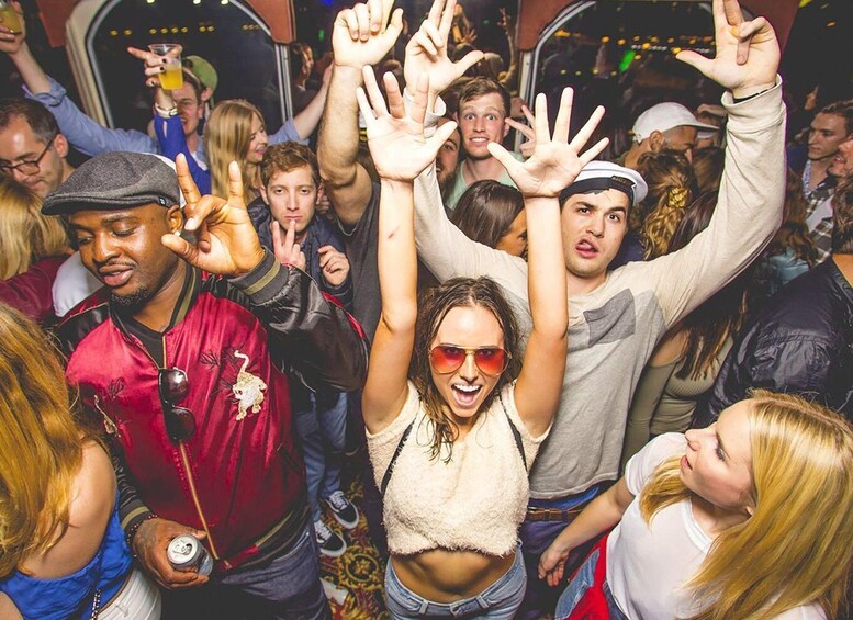 A crowded party with people raising their hands and holding drinks. 4