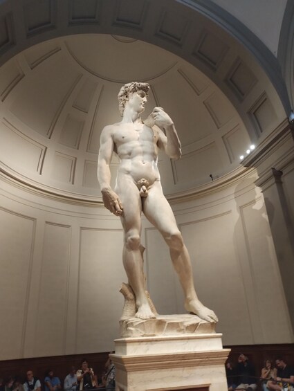 A marble statue of a male figure in classical attire, standing on a pedestal in a grand hall with a high arched ceiling. 3