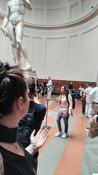 A person taking a photo of a statue in a public indoor space with a crowd in the background. 4