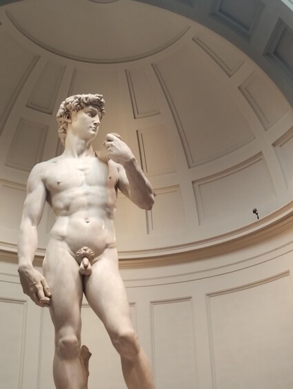 A marble statue of a male figure in classical pose, standing in a grand architectural space with a domed ceiling and decorative moldings. 5