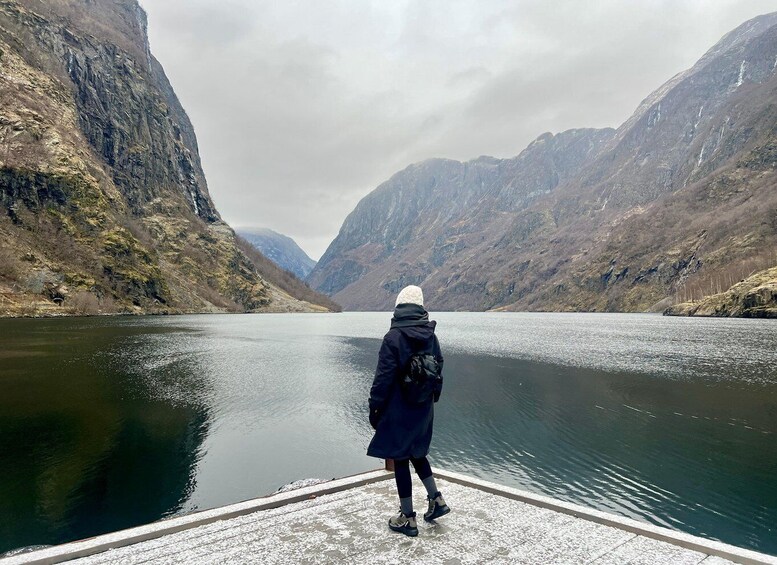 A person standing on a dock overlooking a calm lake surrounded by mountains. 5