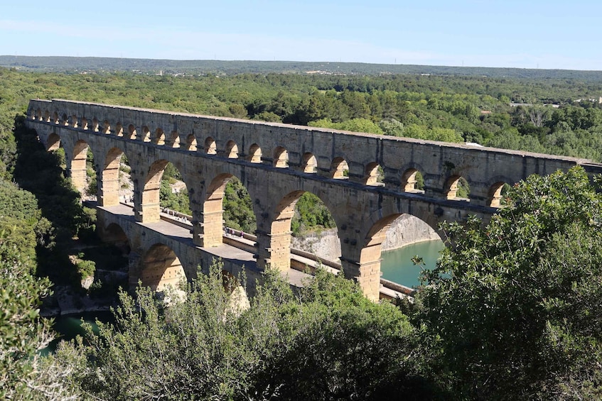 A stone aqueduct with multiple arches spanning a river, surrounded by lush greenery and hills in the background. 5