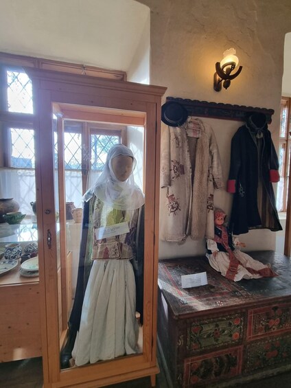 A mannequin in a wooden cabinet, a wall-mounted hat rack, and a decorative chest with intricate patterns. 3