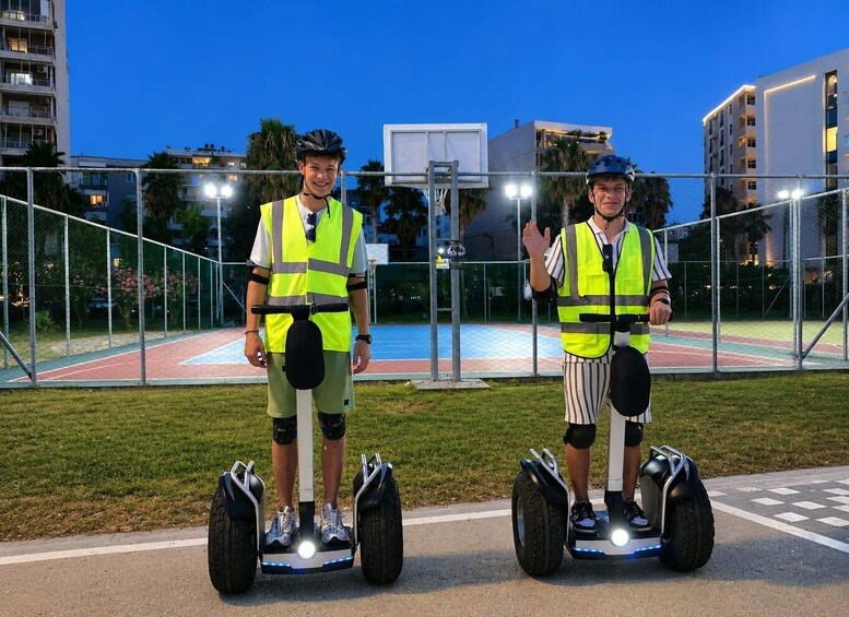 Dos personas en segways en un espacio al aire libre con una cancha de baloncesto y edificios al fondo. 3
