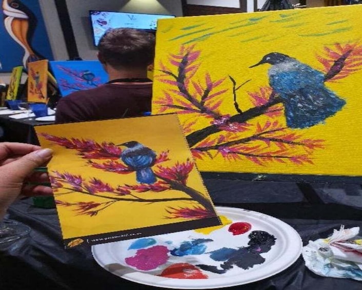 A person holding a painting of a bird on a branch with a yellow background. 1