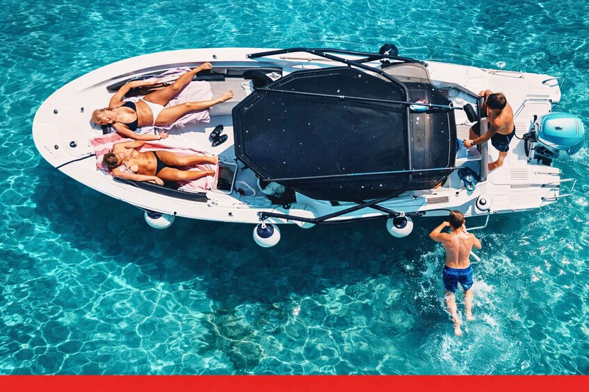 A boat with two people lying on the deck and one person standing in the water. 2