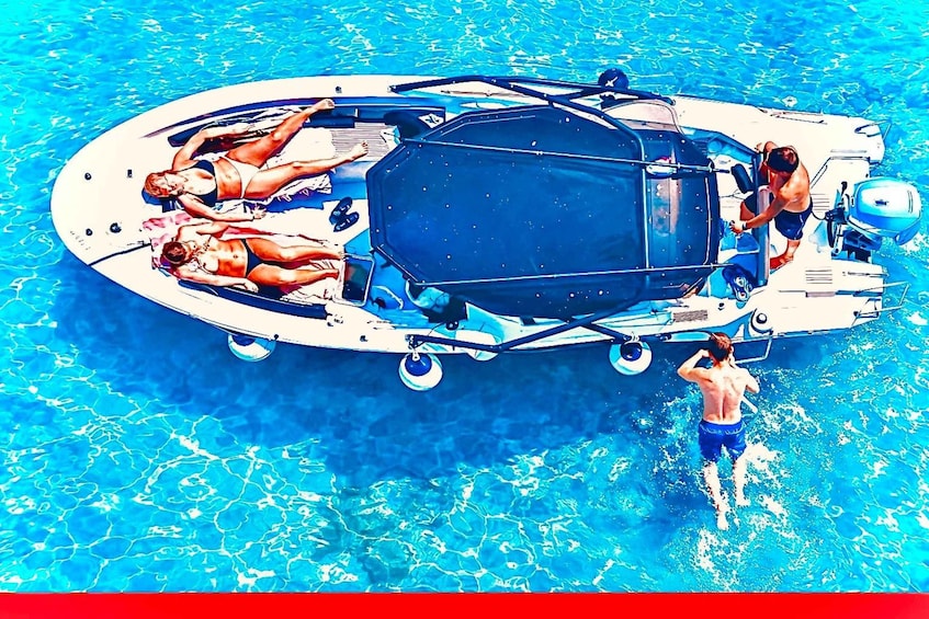 A boat with two people lying on the deck and one person standing in the water. 1