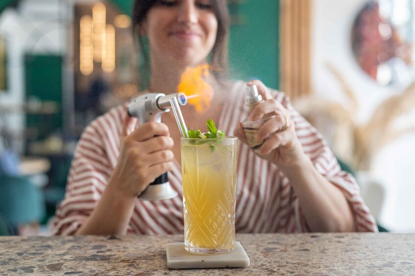 A person preparing a drink with a shaker, a glass, and a mint sprig. 2