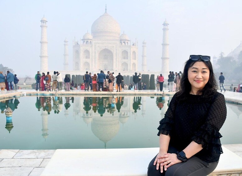 Een persoon zittend voor de Taj Mahal, met het monument weerkaatst in het water. 4