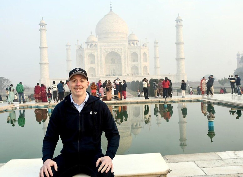 Een persoon zittend voor de Taj Mahal, met het spiegelbeeld ervan in het water. 5