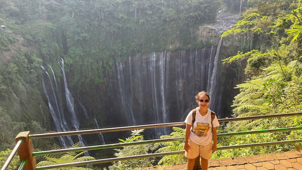 A person standing on a viewing platform with a waterfall in the background. 2