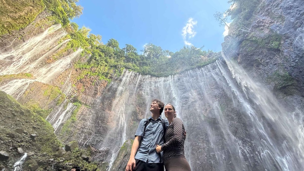 A waterfall with a couple standing in front of it. 1