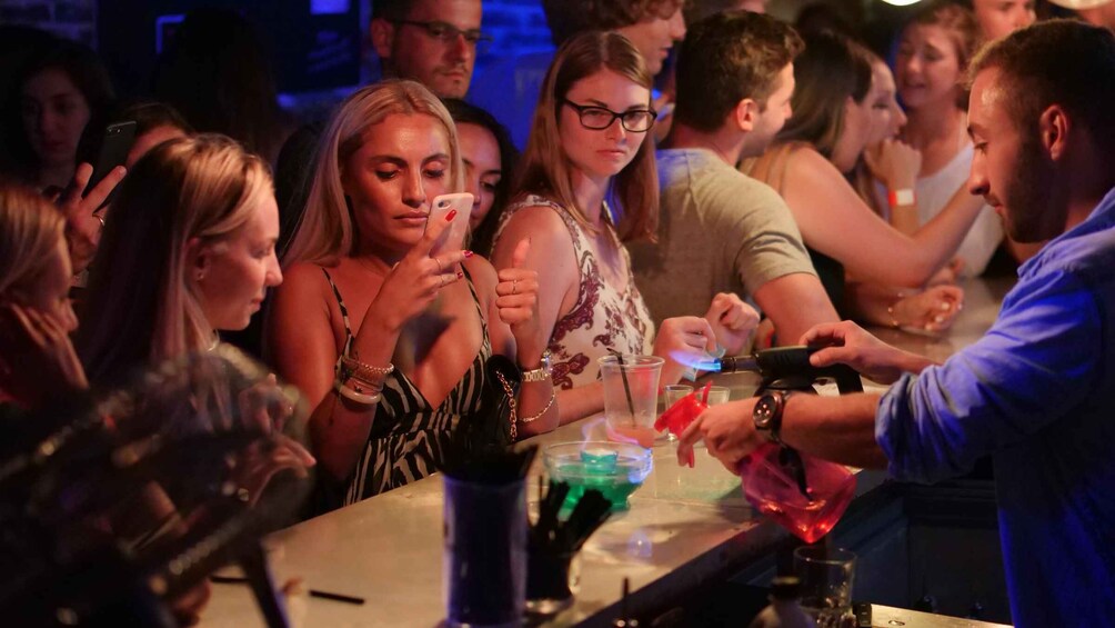 People at a bar with drinks and a bartender preparing a drink. 2