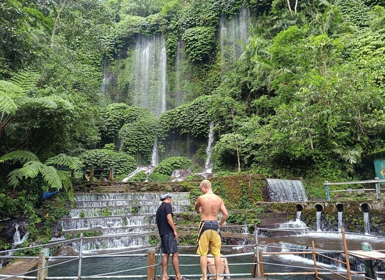A man and a woman standing on a wooden platform overlooking a waterfall in a lush forest. 5