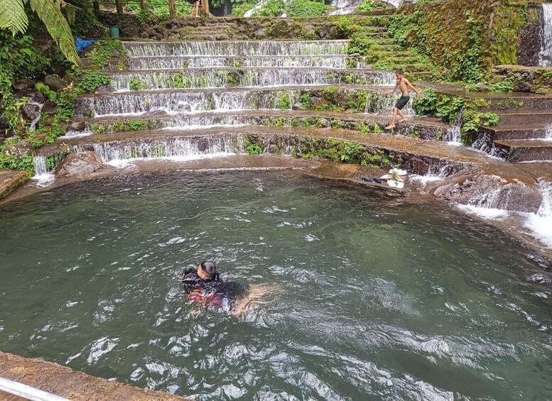 A person swimming in a natural pool with cascading waterfalls in the background. 4