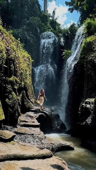 A waterfall in a forested area with a person standing on rocks. 3