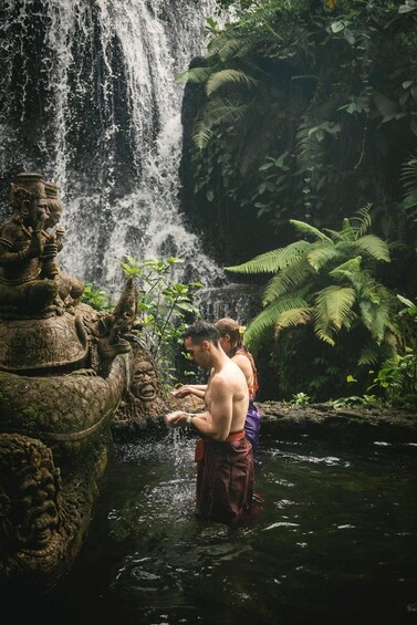 A waterfall, a stone statue, and two people in a natural setting. 2