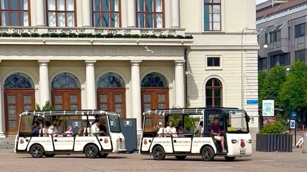 Two sightseeing tour vehicles parked in front of a historic building with ornate doors and columns. 1