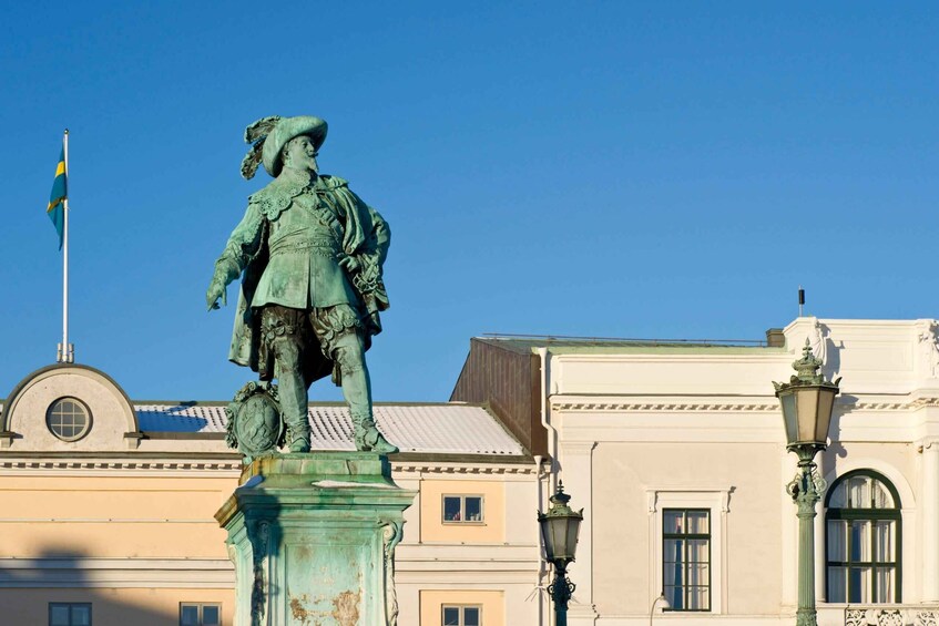 A bronze statue of a historical figure on a pedestal, with a building and a flag in the background. 5