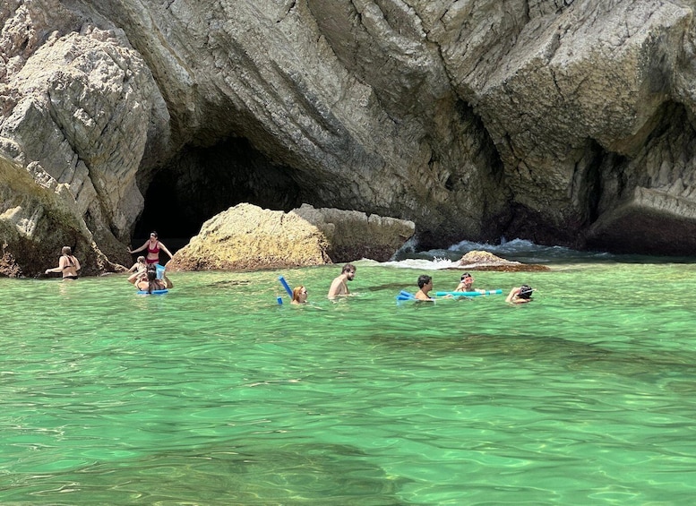 People swimming and floating in clear water near a rocky cave entrance. 4