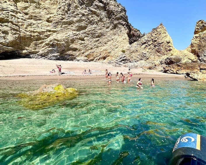 A clear shallow water body with people swimming and sunbathing on a rocky beach. 5