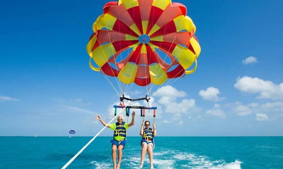 Two people parasailing over turquoise water with a clear sky. 1