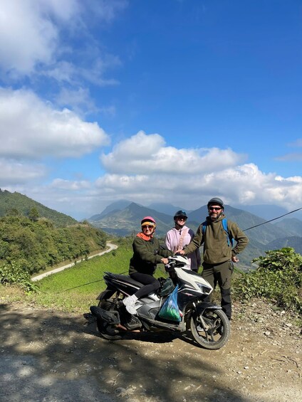 Three people on a dirt road with a scenic mountainous landscape in the background. 4