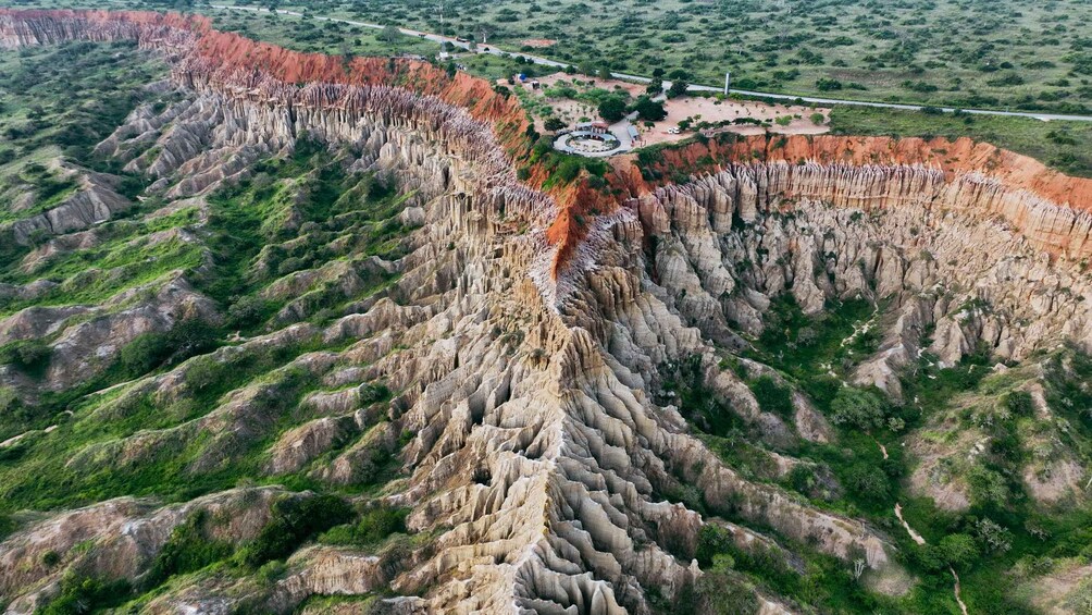 A large, rugged canyon with steep, layered rock formations and a small park area with pathways and structures. 2