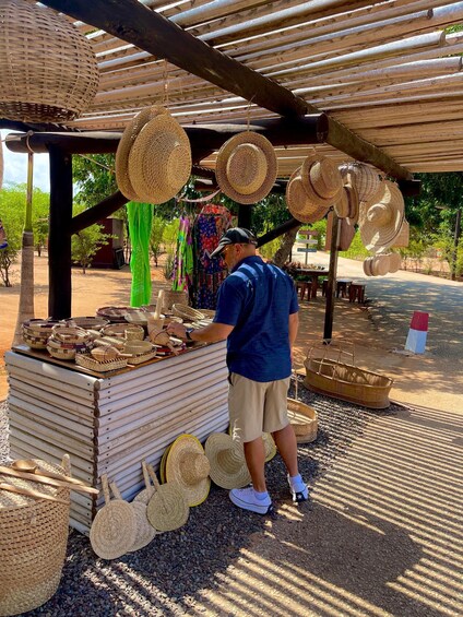 A man arranging woven baskets and hats under a wooden structure. 3