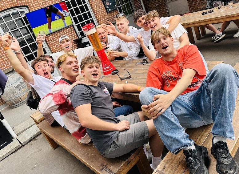 A group of people sitting at a wooden table outdoors, celebrating with a large beer mug. 1