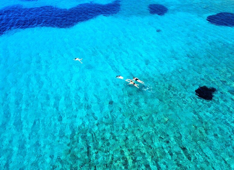 A clear blue sea with three people swimming. 3