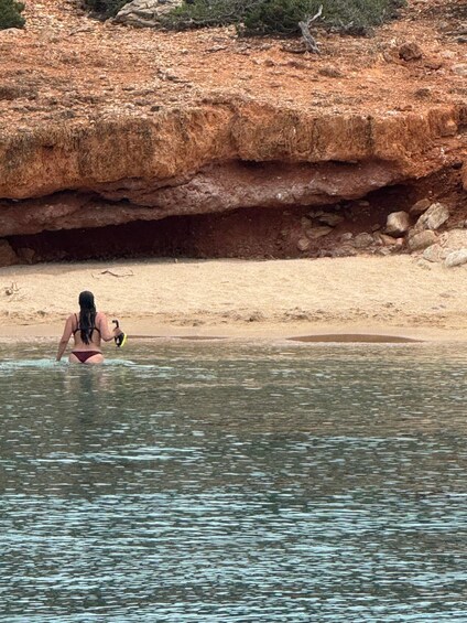 A person in a bikini standing in shallow water near a rocky shore. 4