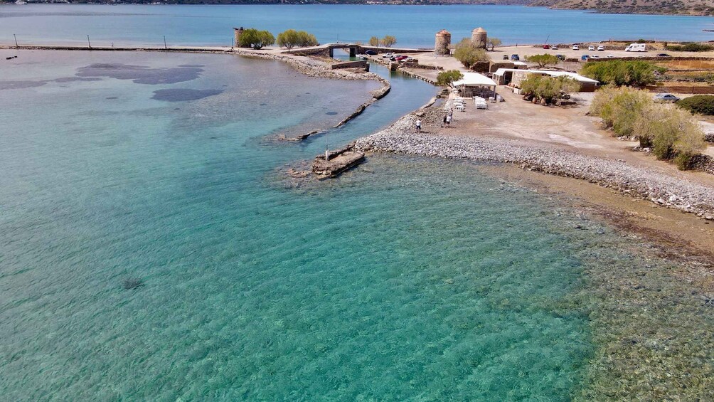 A coastal area with clear turquoise waters, a rocky shoreline, and a few buildings and vehicles. 2
