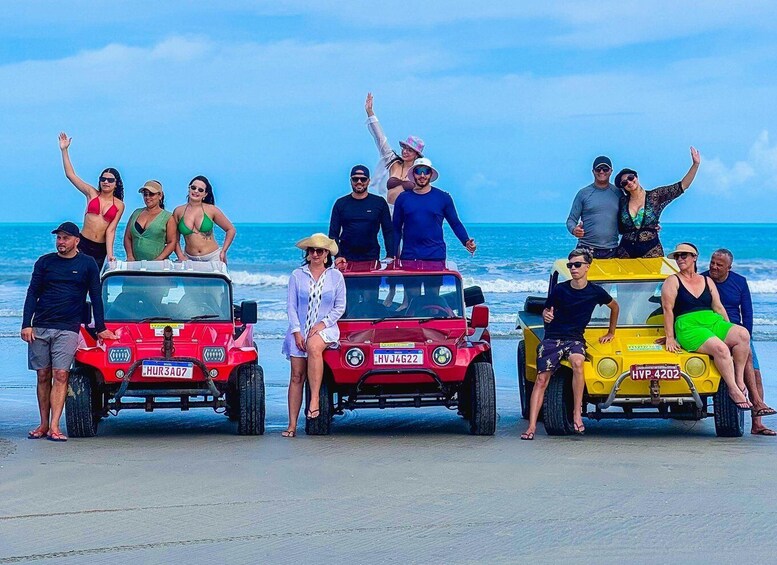 A group of people posing with three off-road vehicles on a beach. 3