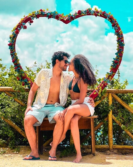 A couple sitting on a bench with a heart-shaped decoration made of flowers and leaves. 5