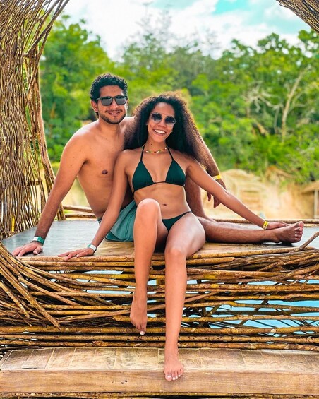 Two people sitting on a woven bench outdoors. 4