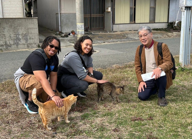 Three people interacting with a cat on a street. 1