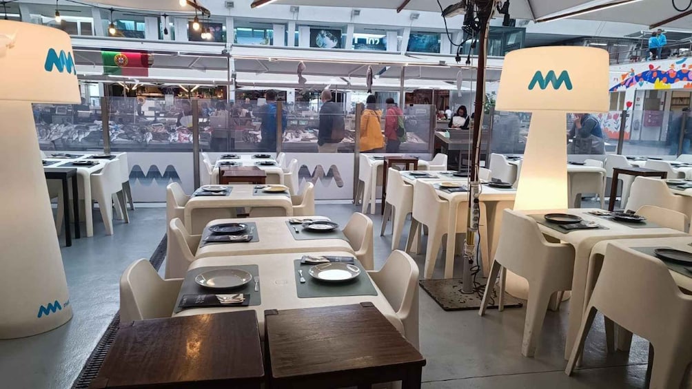 A modern restaurant with white tables and chairs, large lamps, and a view of the city through large windows. 1