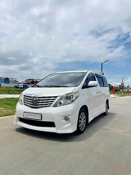 A white minivan parked on a concrete surface with a cloudy sky in the background. 1
